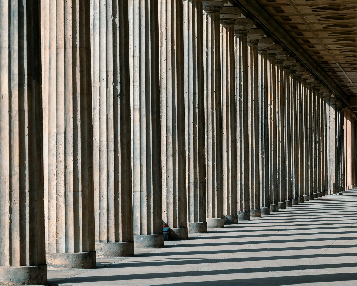 Long colonnade of fluted stone columns casting parallel shadows across the pavement
