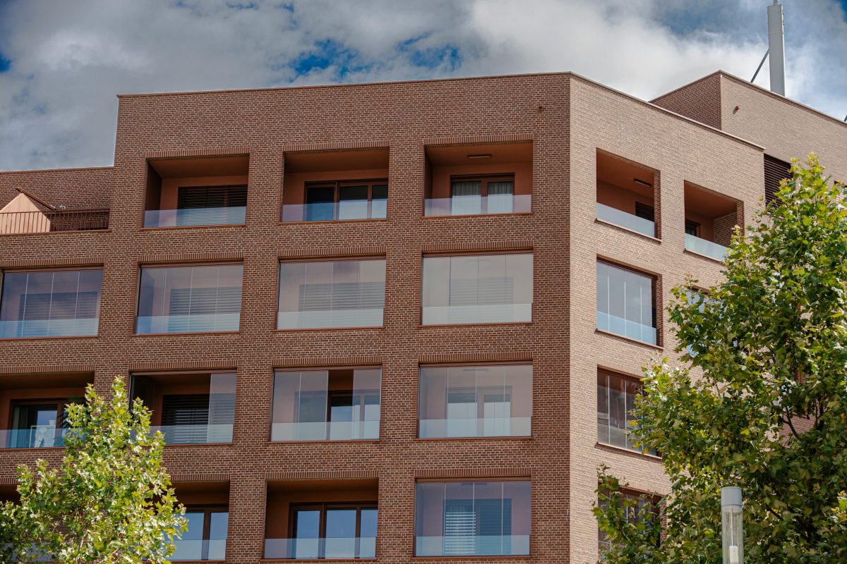 Modern brick apartment building with glass-fronted balconies framed by green trees