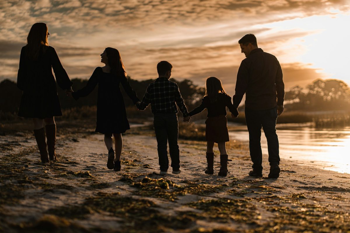 A family of five walking hand in hand along a beach at sunset, seen in silhouette