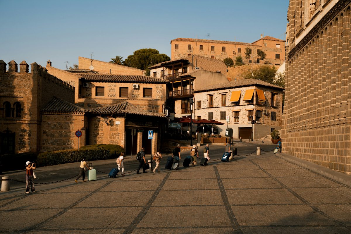 Travellers pulling suitcases across a sunlit stone square in an old European town